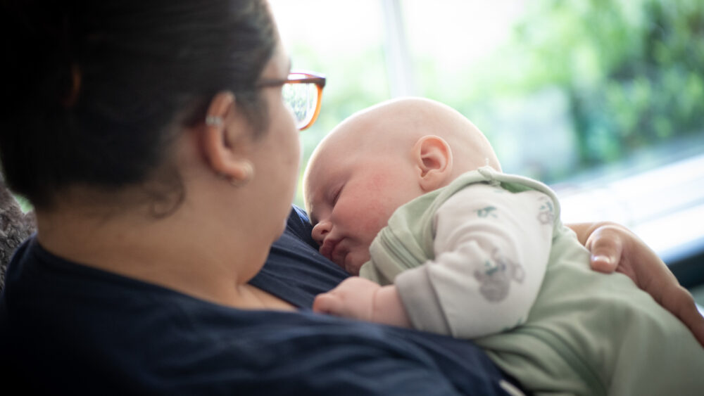 4 Expert Tips to Help Your Child Adjust to Daylight Saving Time 11 A baby in a green onesie is asleep in the arms of a woman.