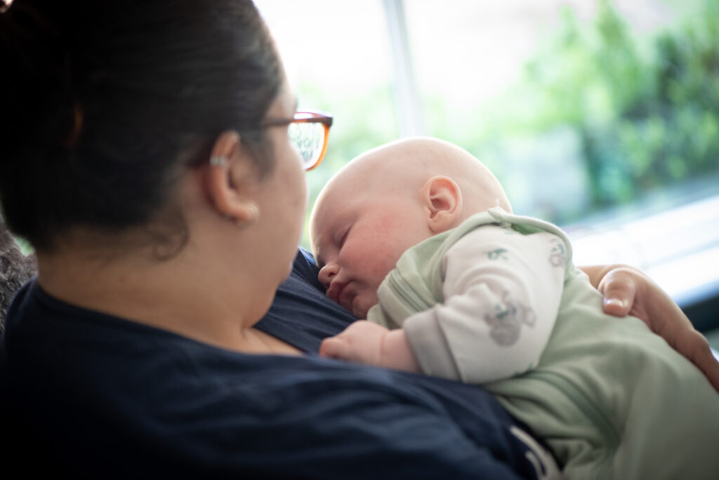 4 Expert Tips to Help Your Child Adjust to Daylight Saving Time 9 A baby in a green onesie is asleep in the arms of a woman.